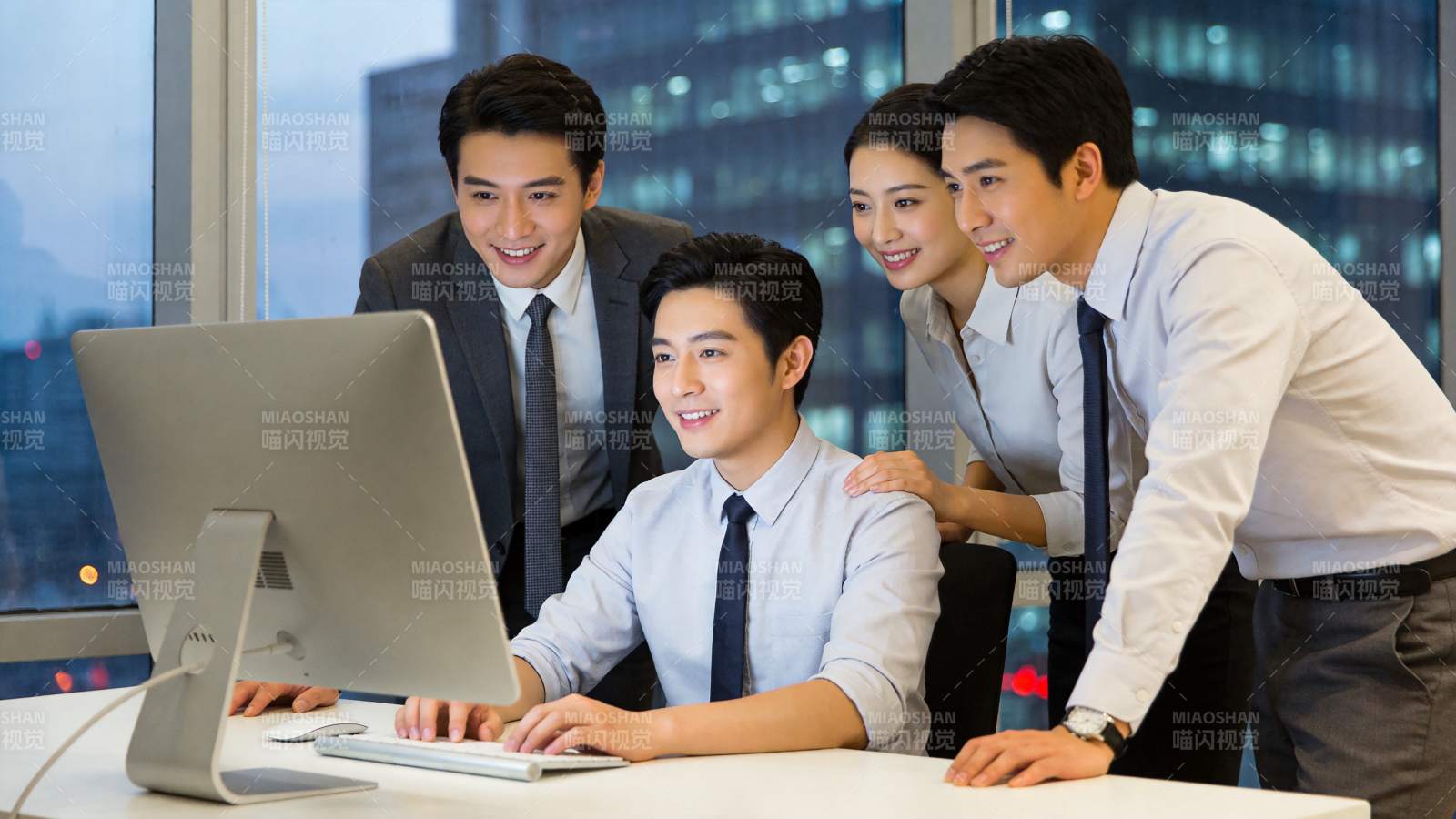 四位职场人员围看电脑屏幕讨论工作内容图片