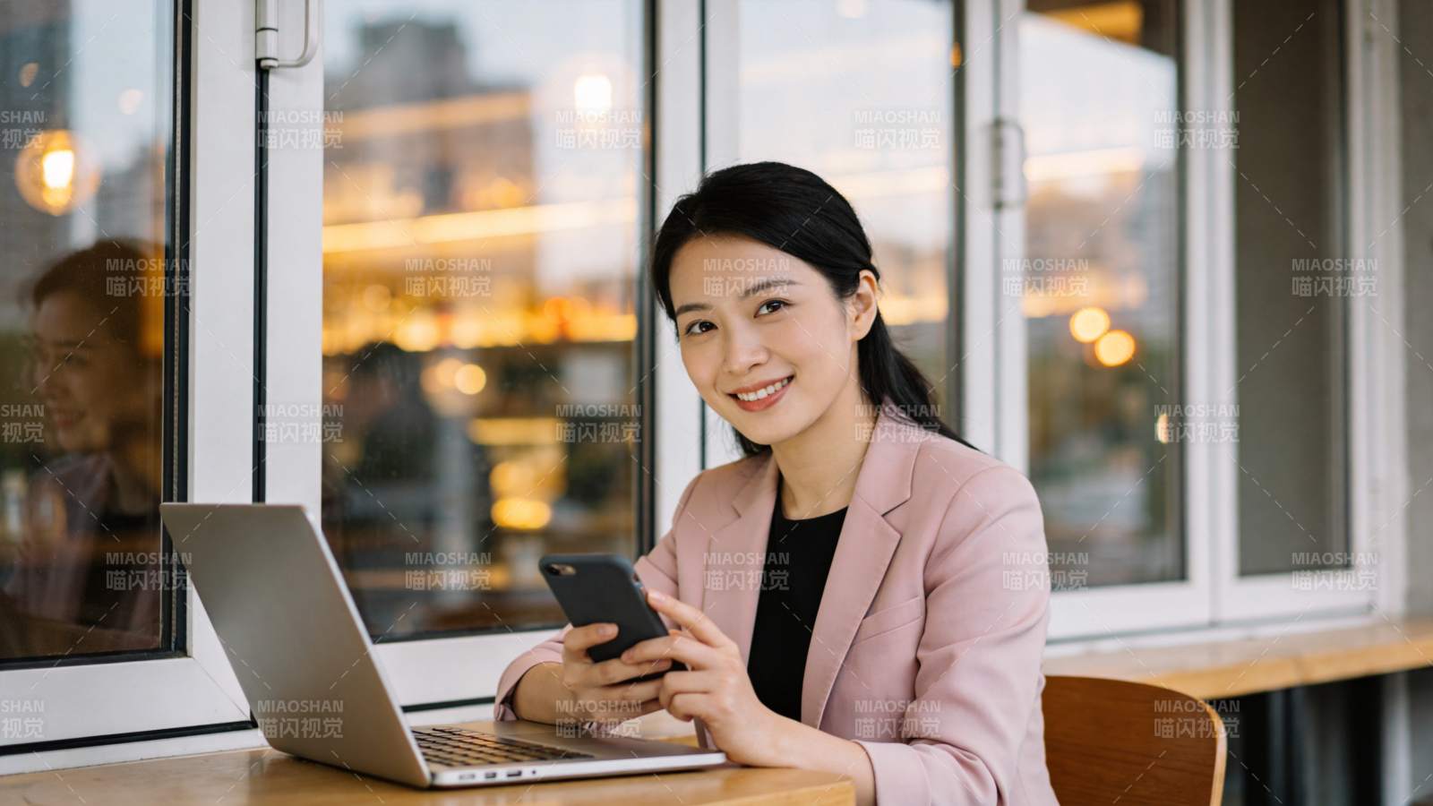 女性在窗边使用笔记本电脑与手机工作图片