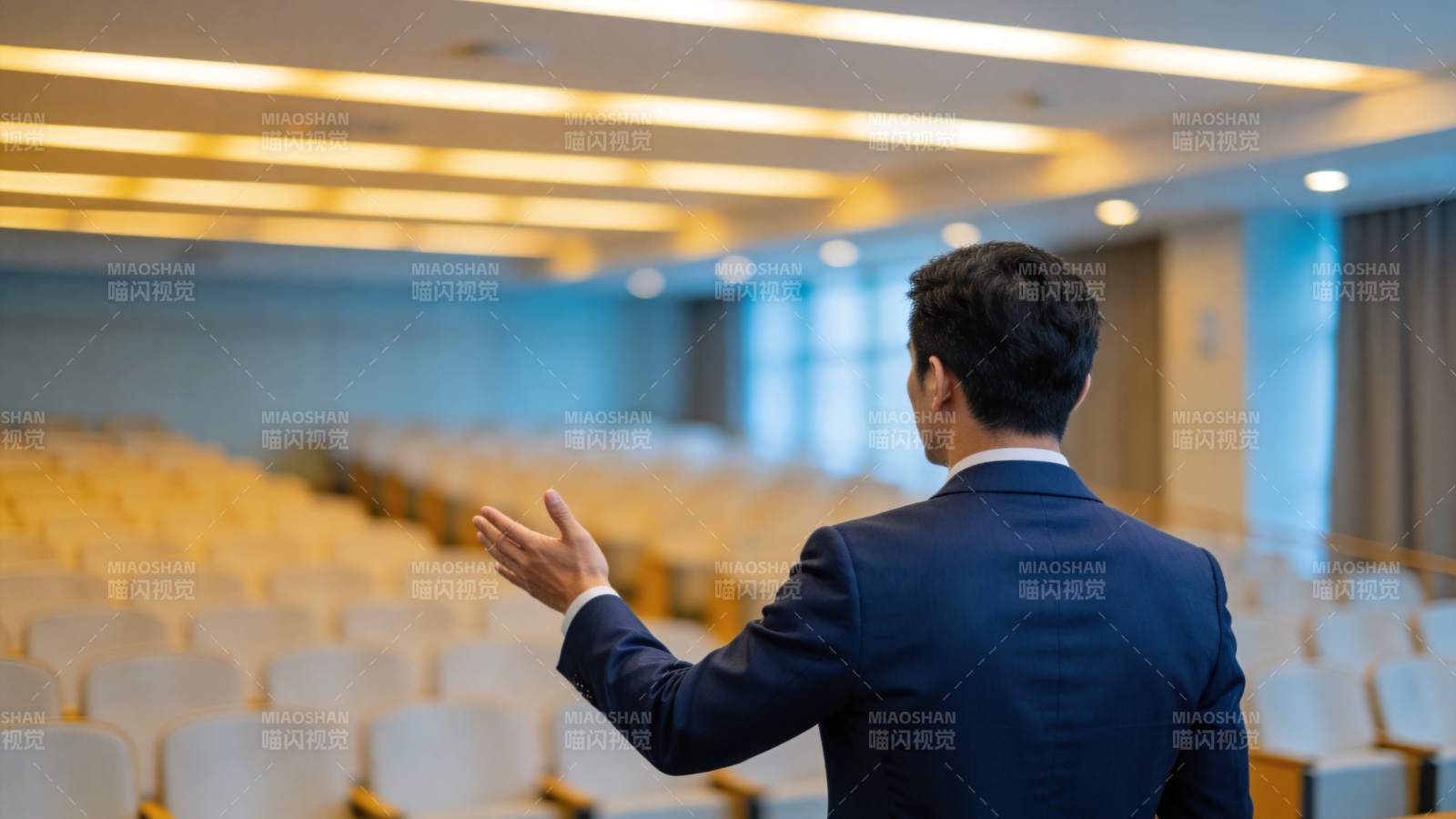西装男子背对镜头在空会议厅演讲手势图片