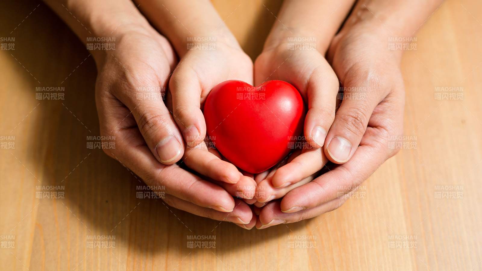 双手捧着红色心形物体置于木桌之上图片
