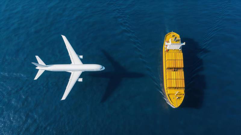 白色客机与黄色货轮在蓝色海面并行航行图片