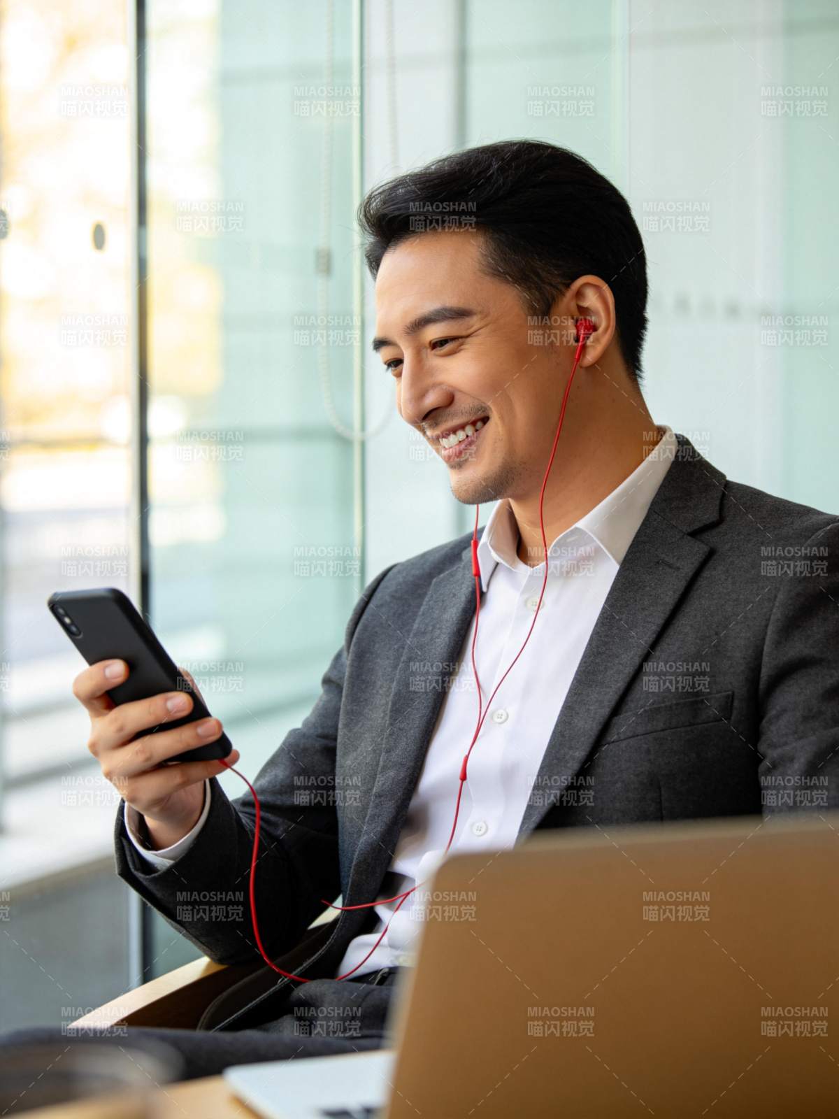 穿西装男子戴红耳机看手机微笑图片