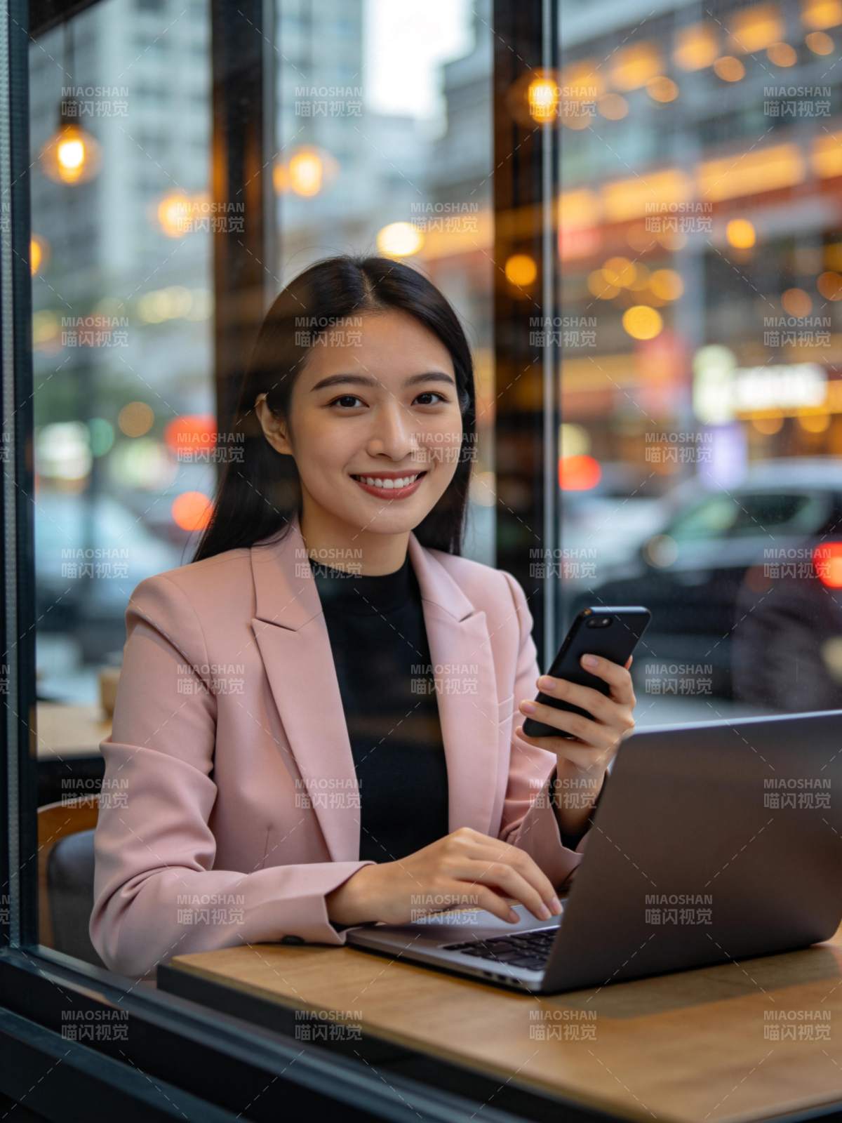 女性在窗边使用笔记本电脑与手机工作图片