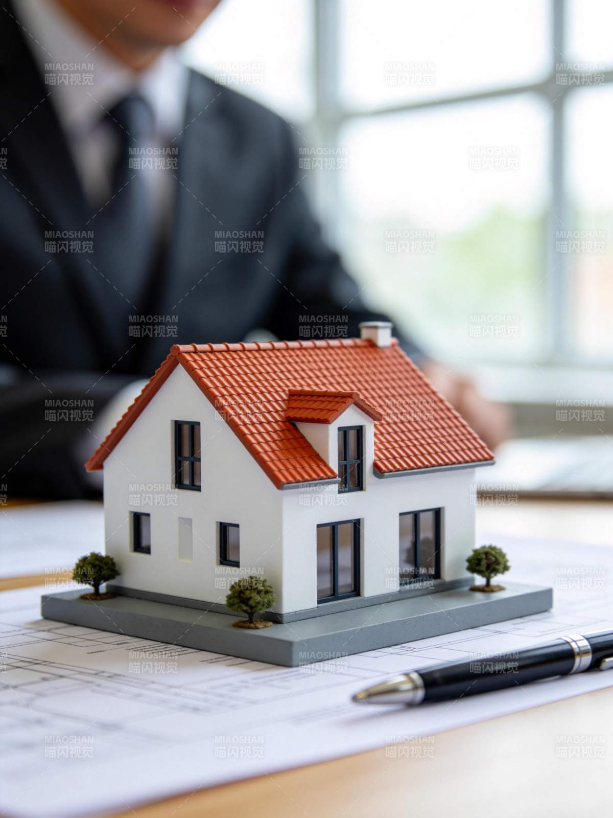 西装男子桌前摆放房屋模型与图纸图片