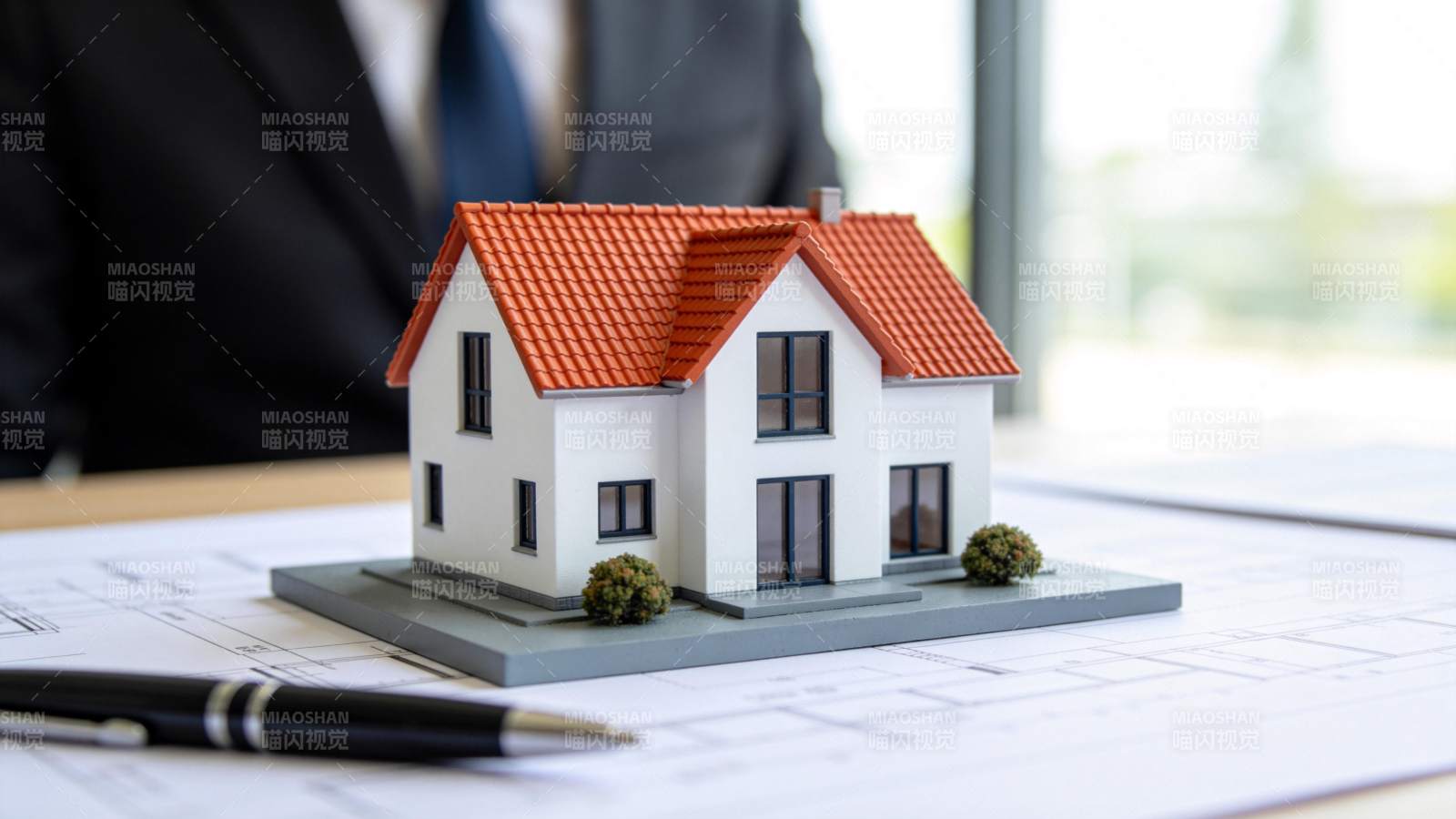 白色模型房屋置于建筑图纸与钢笔旁图片