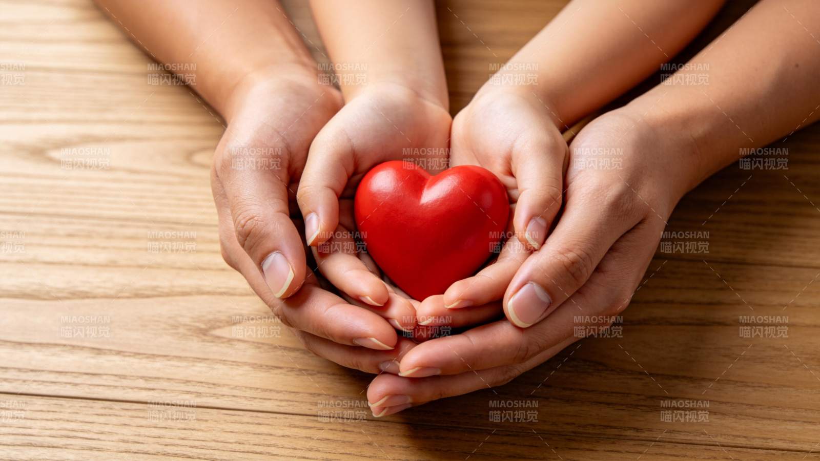 多双手共同托举红色心形物体置于木桌图片
