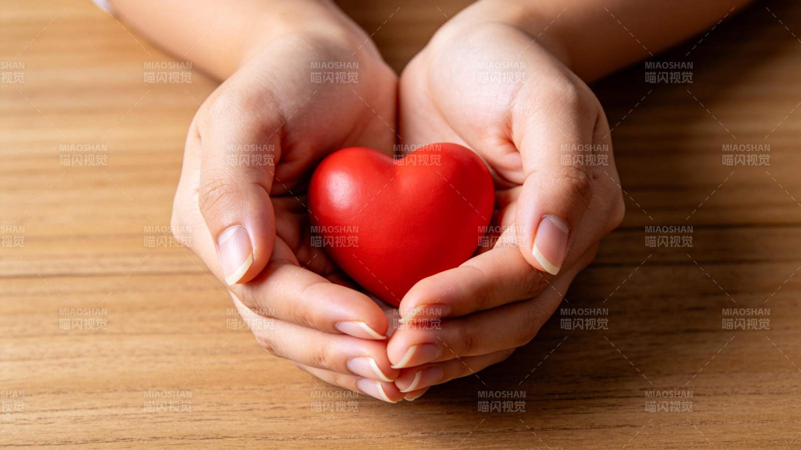 双手捧着红色心形物体置于木桌之上图片
