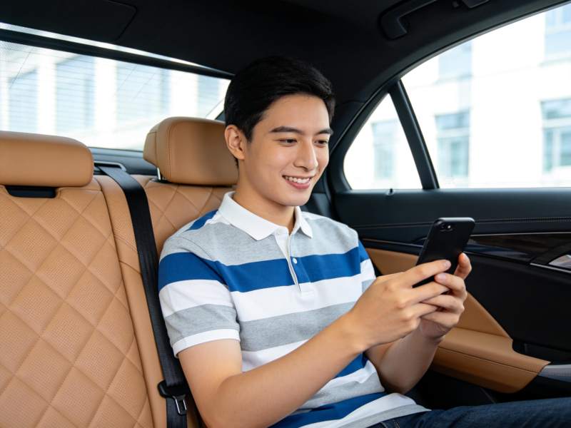 年轻男子坐在汽车后座使用智能手机图片