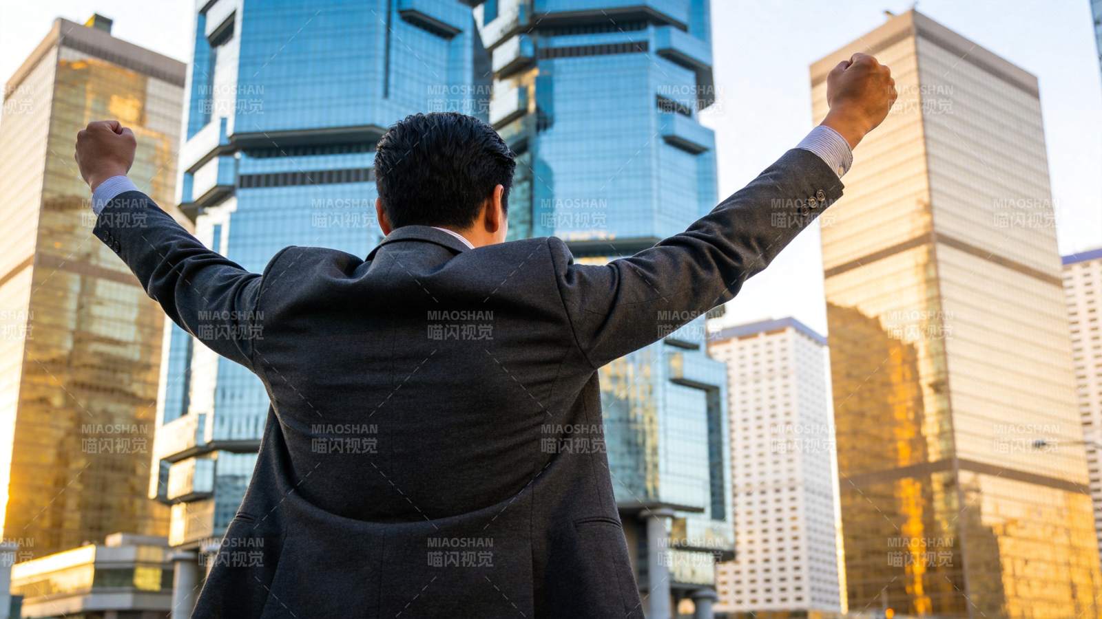 西装男子背对镜头双臂高举于城市高楼间图片