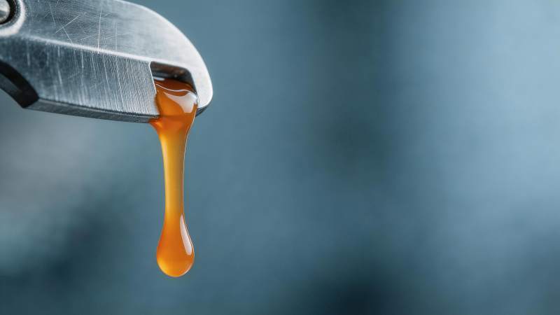 金属钳口滴落琥珀色黏稠液体特写图片