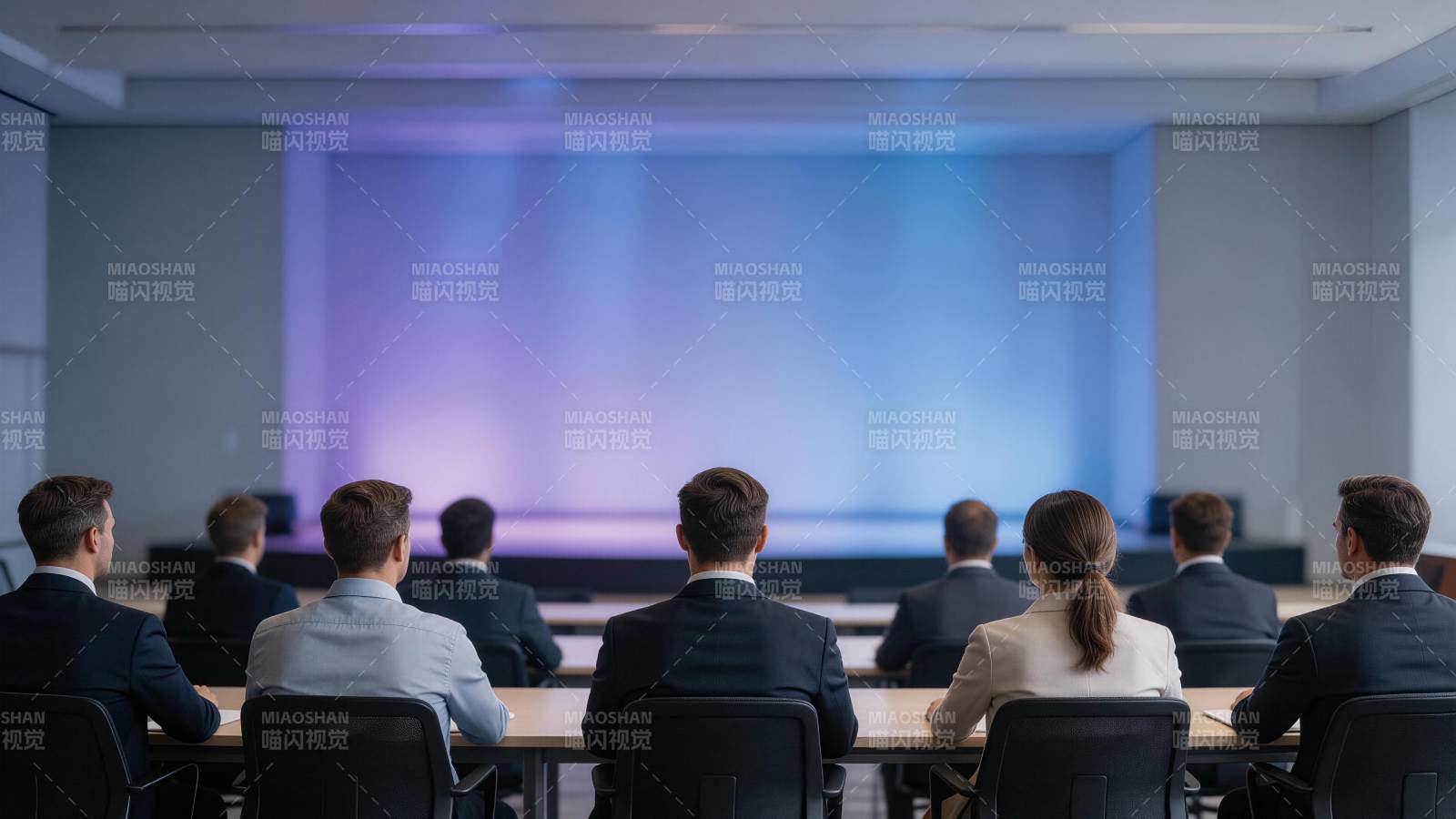 多人背对镜头坐在会议桌前观看舞台投影图片