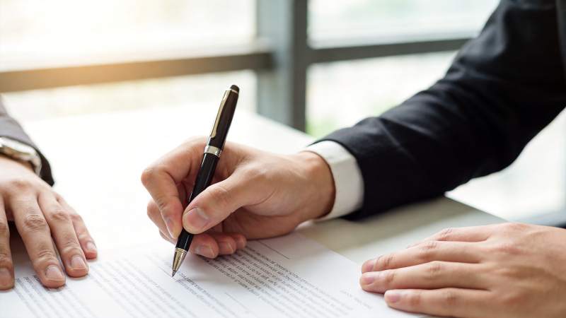 商务人士手持钢笔签署文件特写图片