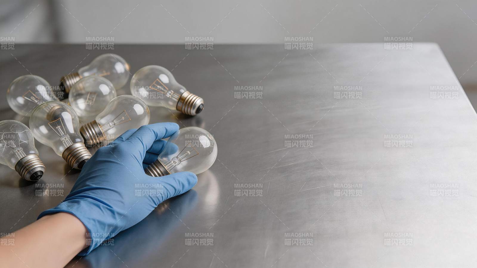 戴蓝色手套的手握白炽灯泡置于金属台面图片
