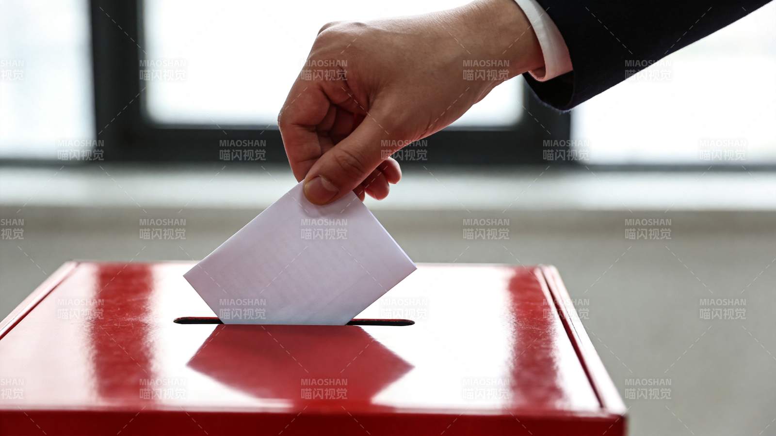 手将选票投入红色投票箱的特写画面图片