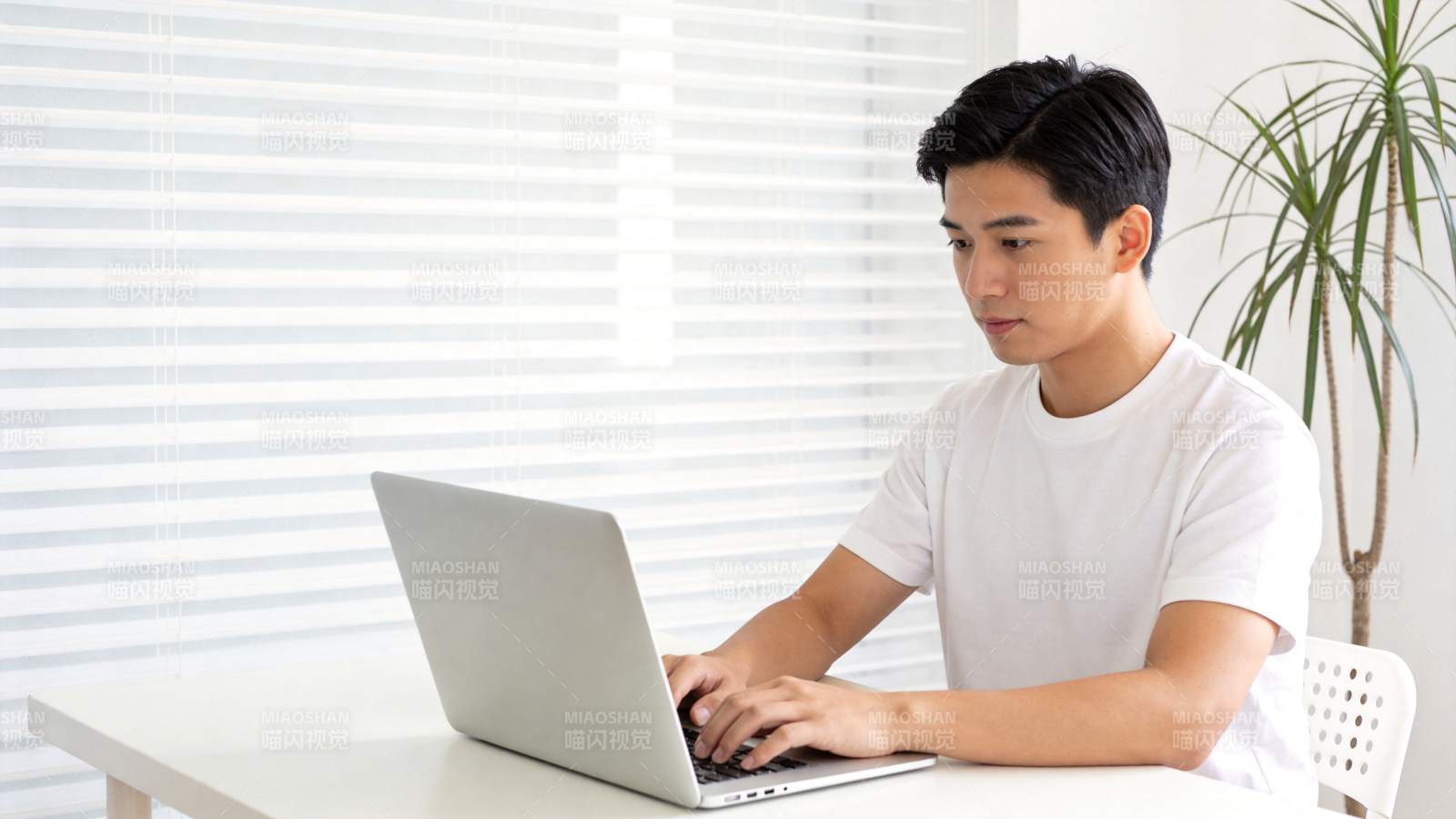青年男子在白色桌前使用银色笔记本电脑图片