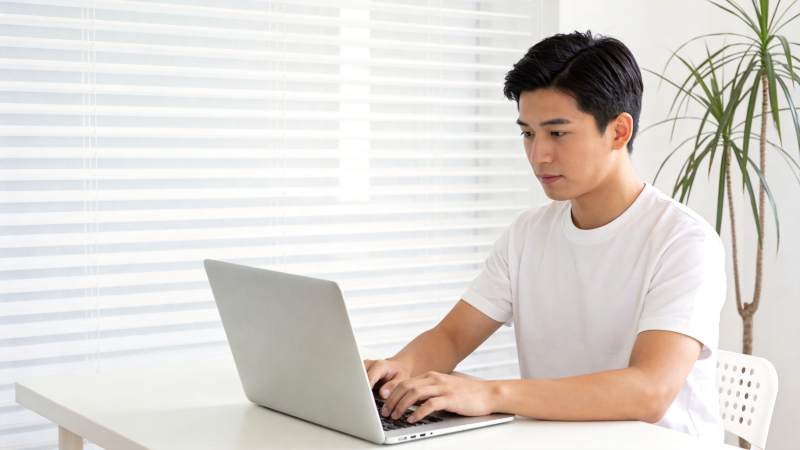 青年男子在白色桌前使用银色笔记本电脑图片