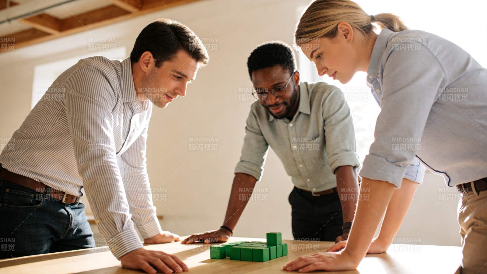 三人围桌专注观察绿色积木搭建结构图片