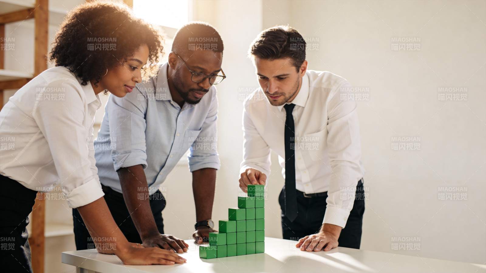 三位职场人士围绕绿色积木进行协作讨论图片