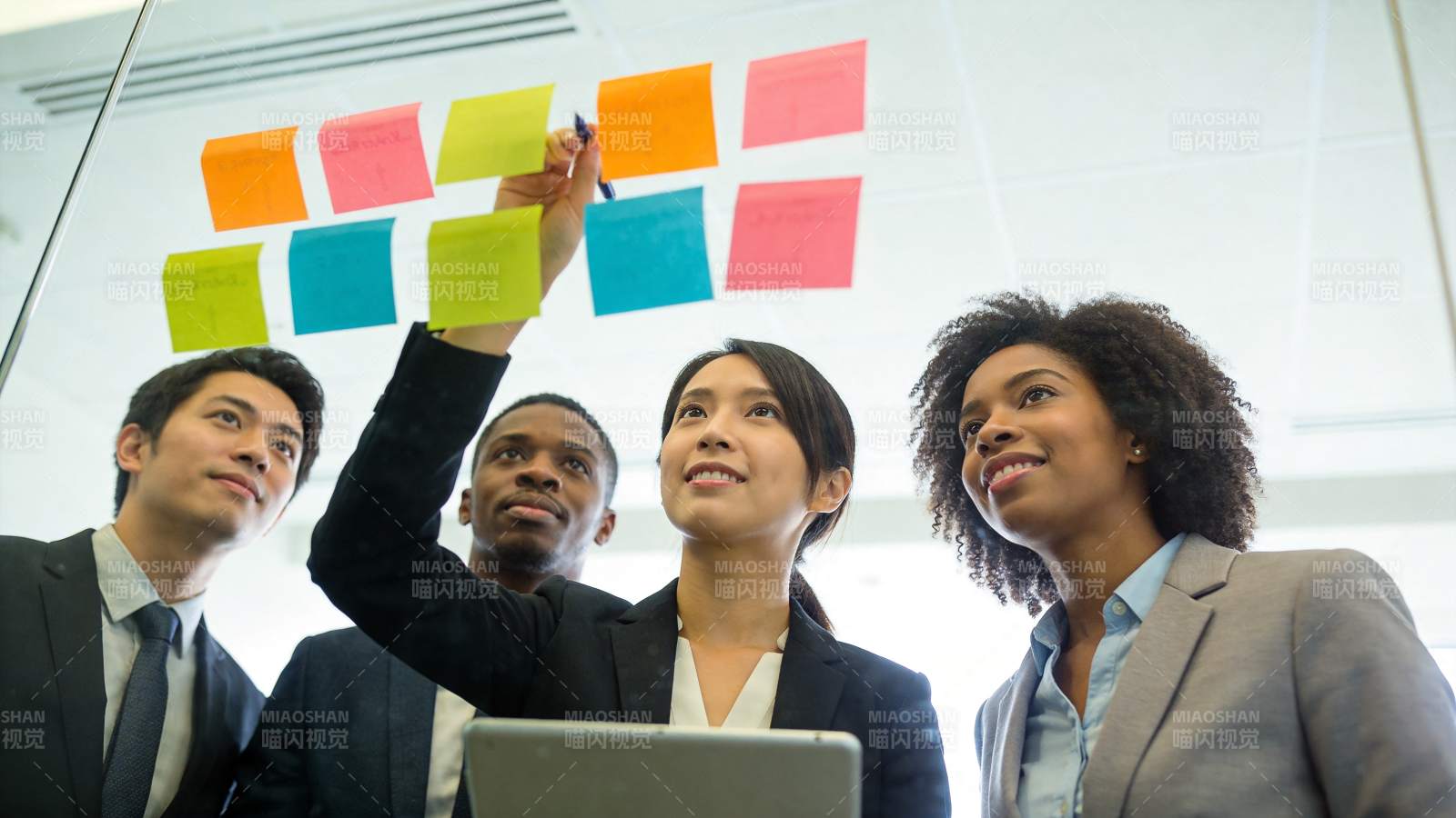 四人协作在玻璃板贴彩色便签讨论工作图片