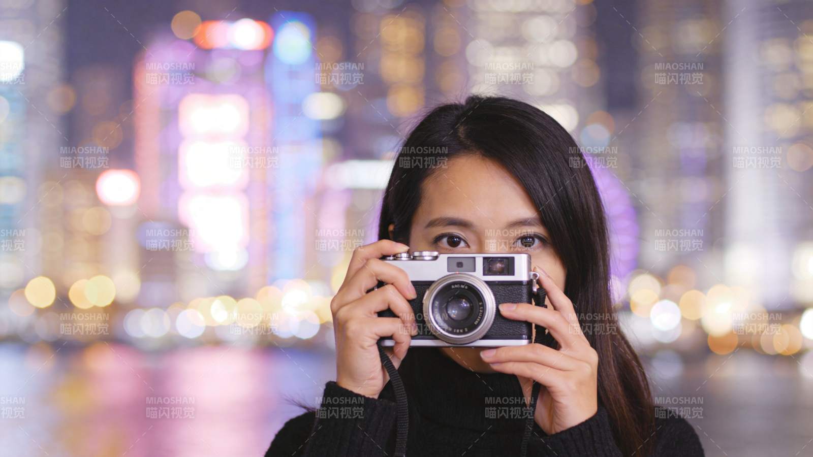 女子手持胶片相机拍摄夜景城市灯光图片