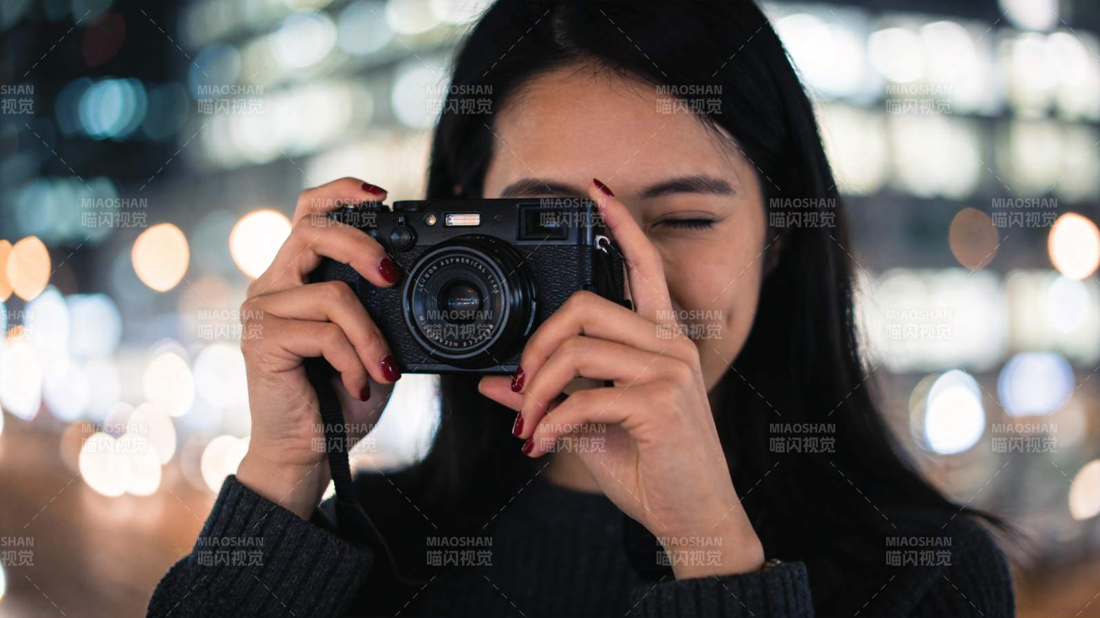 黑衣女子手持相机夜间拍摄城市灯光图片