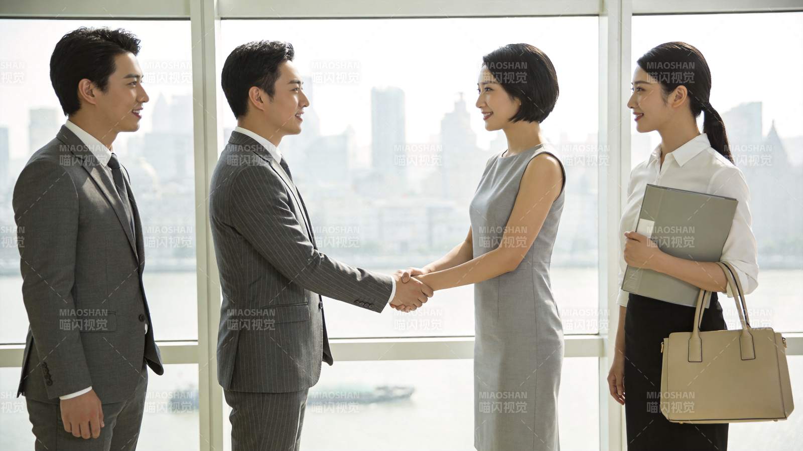 四位职场人士在窗边握手交流场景图片