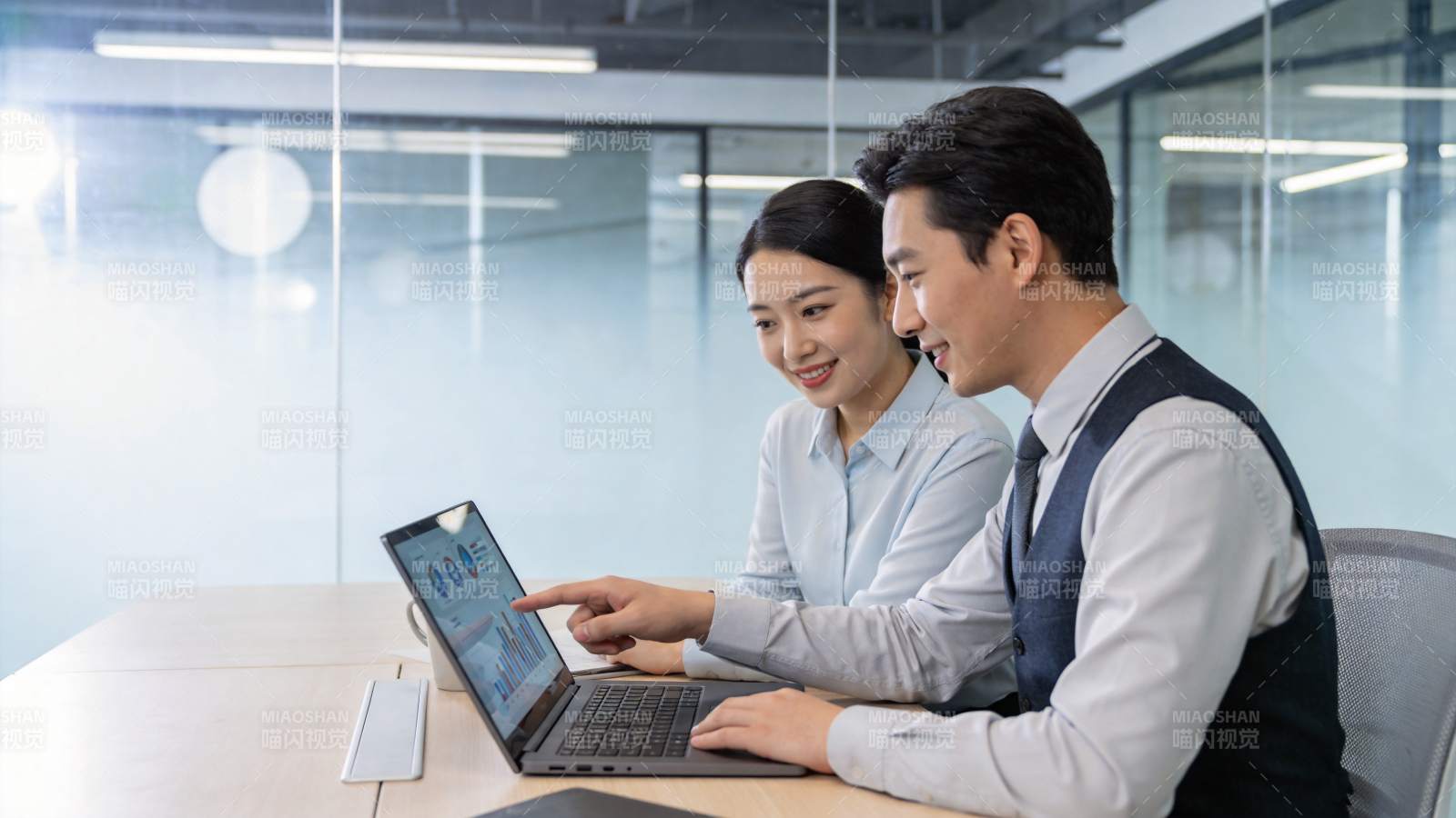 办公室内两人协作查看笔记本电脑数据图表图片
