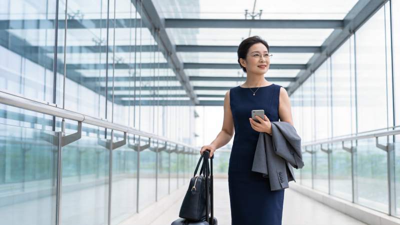 穿深蓝连衣裙女子手提行李箱行走于玻璃廊桥图片