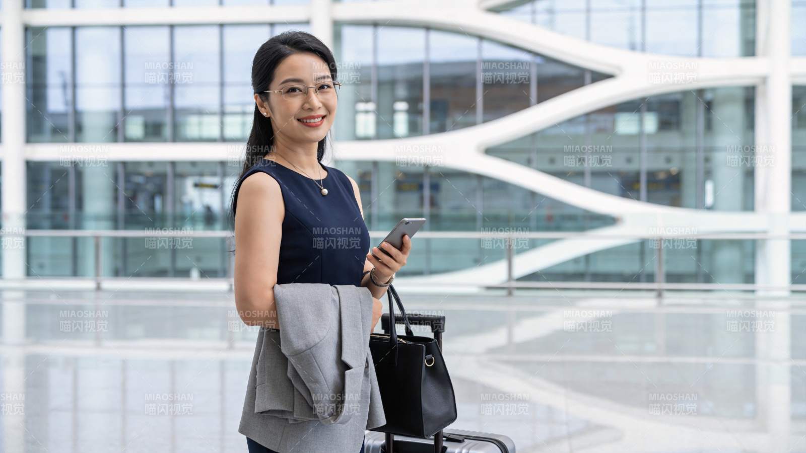 戴眼镜女性手持手机站在现代建筑大厅内图片