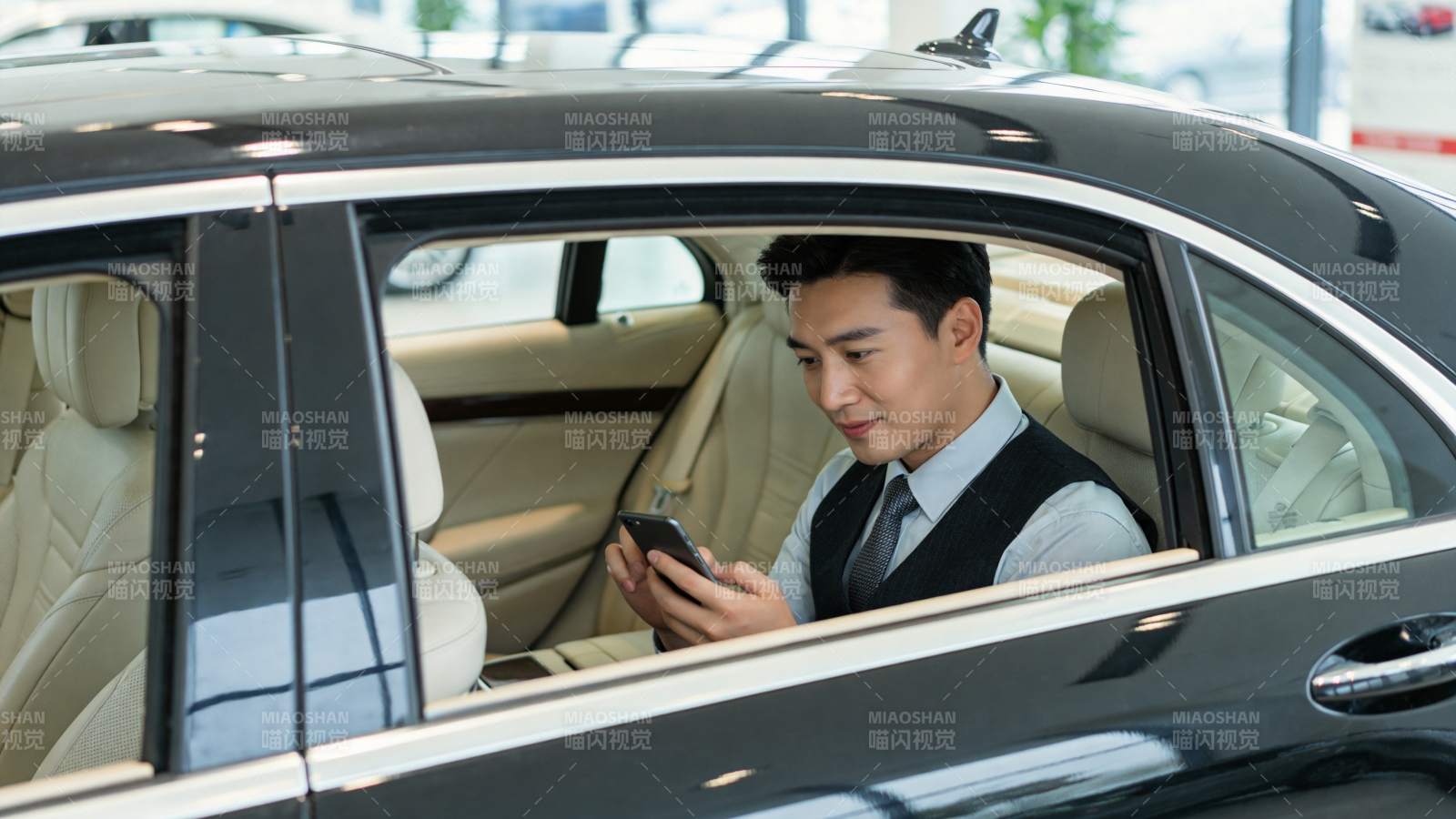 男士坐于黑色轿车内专注使用智能手机图片