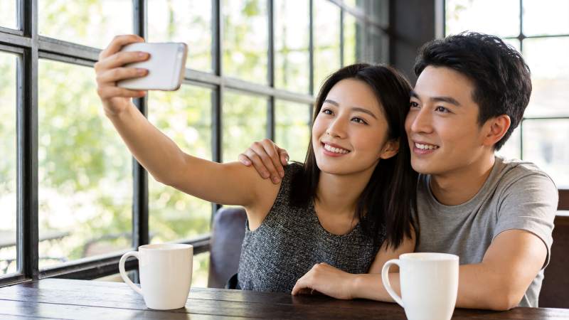 男女在窗边咖啡馆用手机自拍合影图片