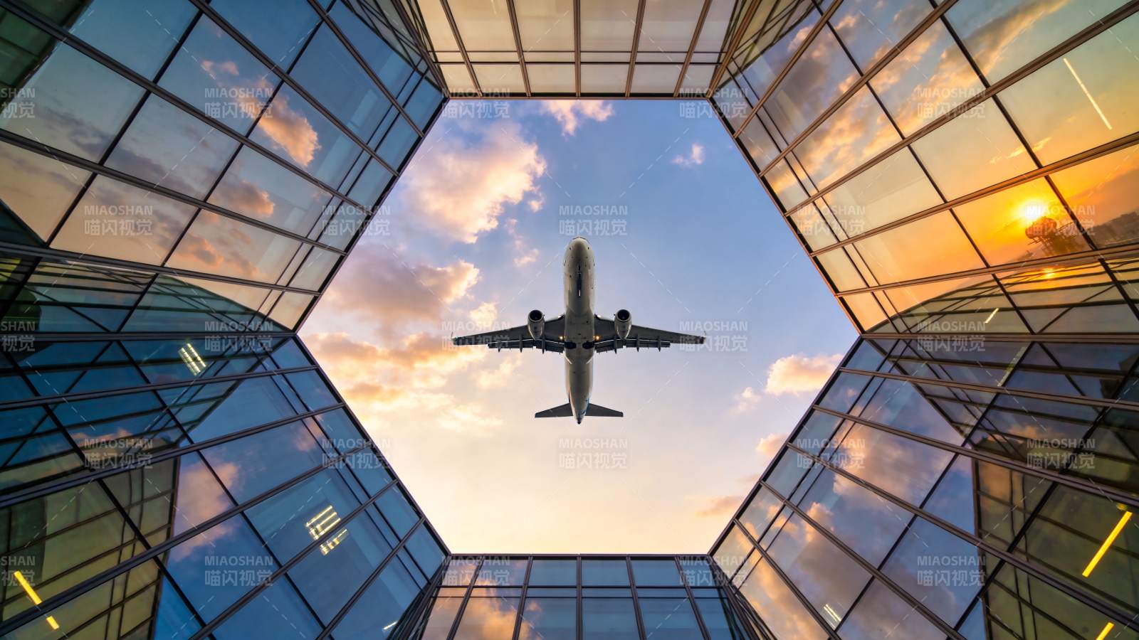 玻璃幕墙间飞机掠过夕阳天空图片