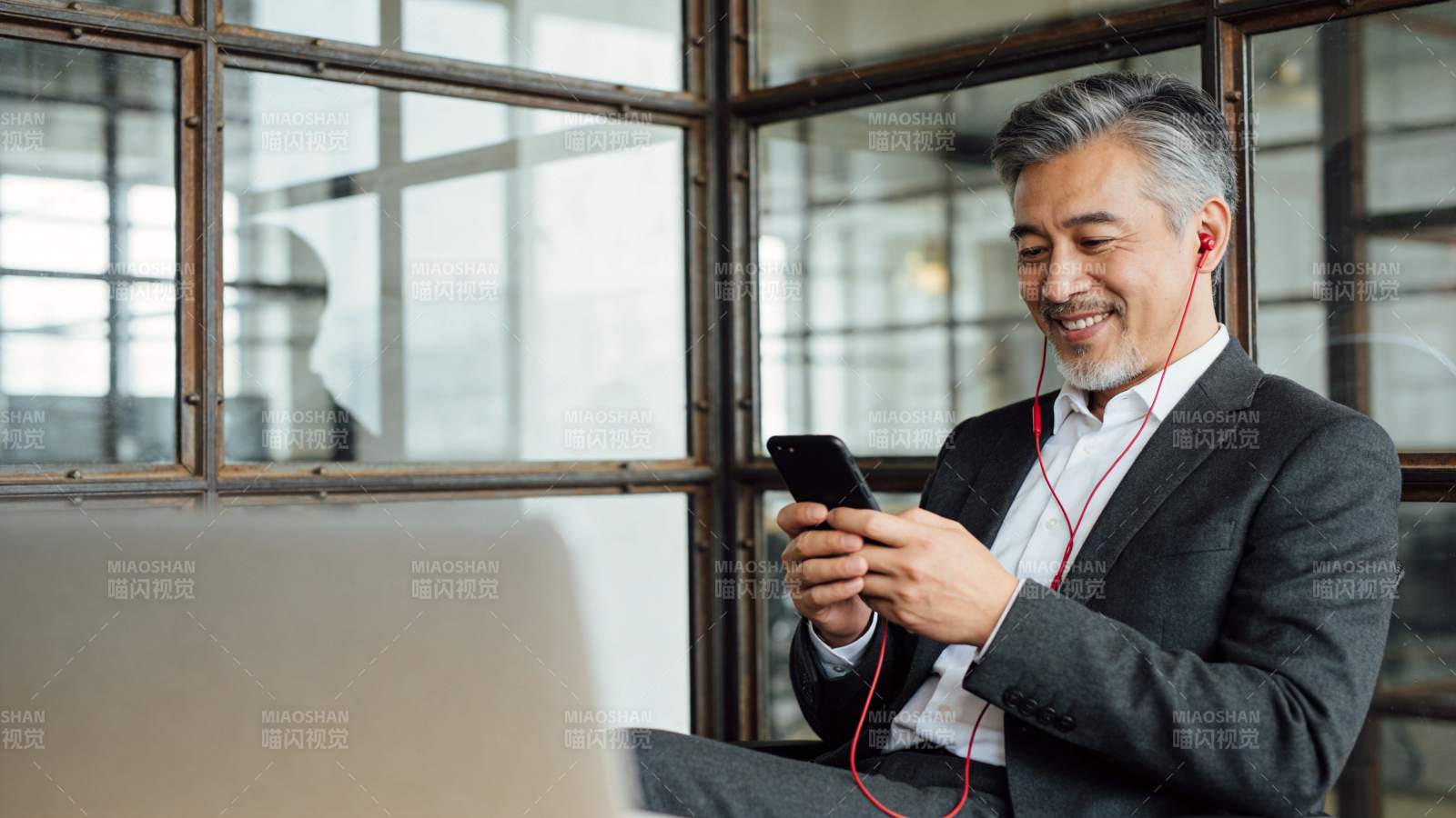 中年男子戴耳机使用手机微笑办公场景图片
