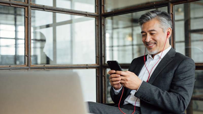 中年男子戴耳机使用手机微笑办公场景图片