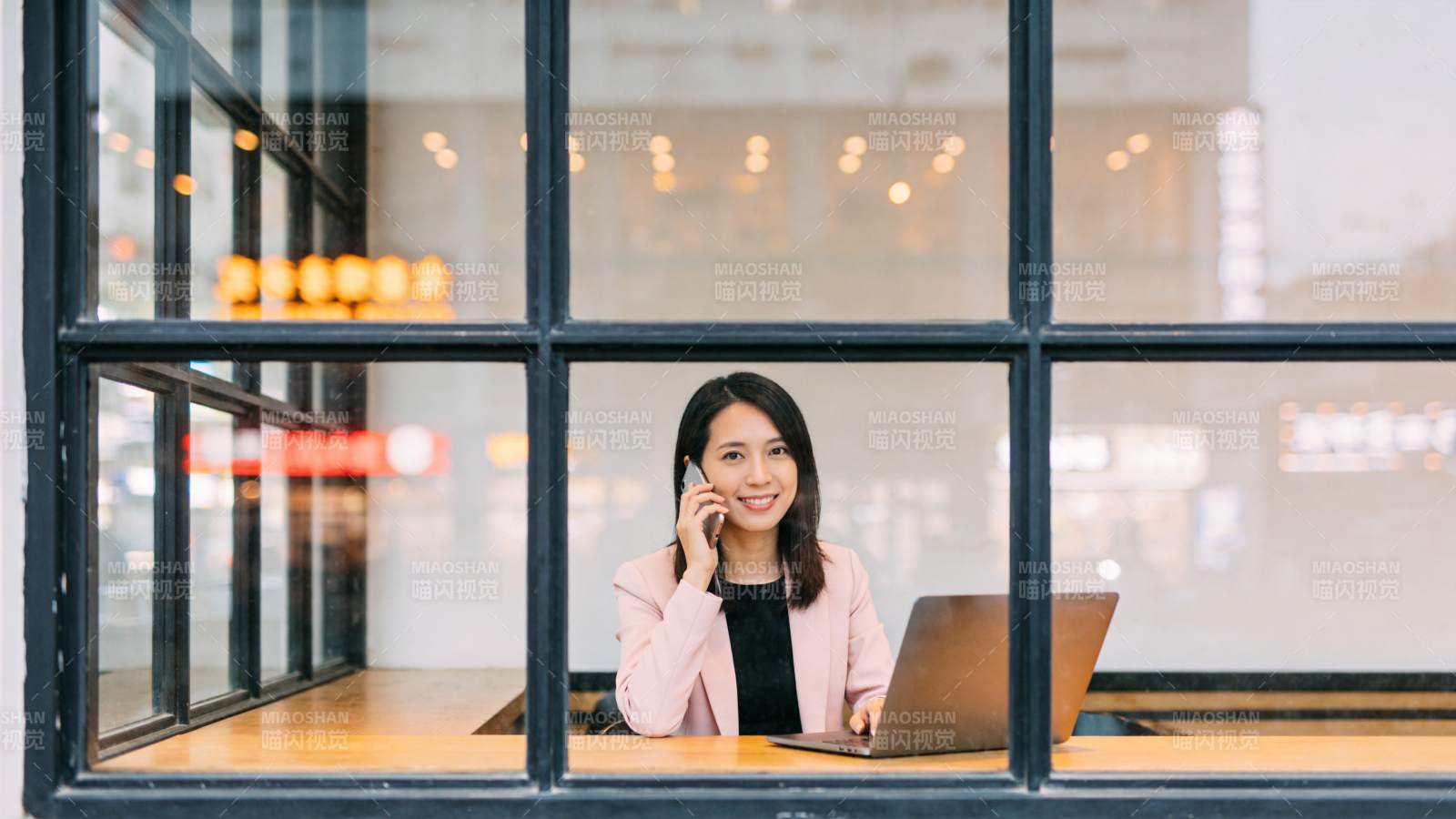 女性在窗边使用笔记本电脑打电话图片
