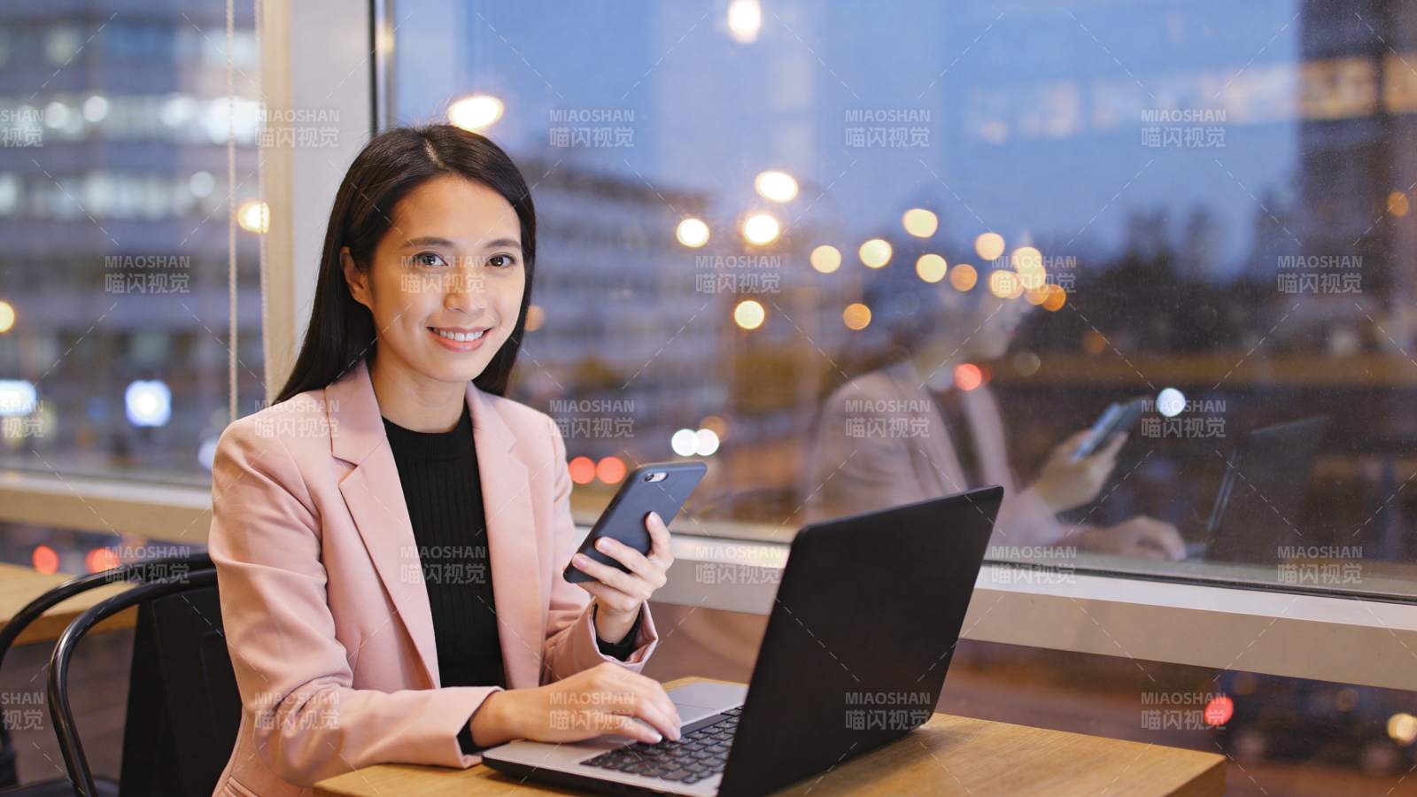 女性在窗边使用笔记本电脑与手机工作图片