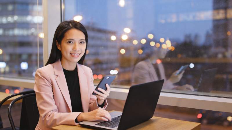 女性在窗边使用笔记本电脑与手机工作图片