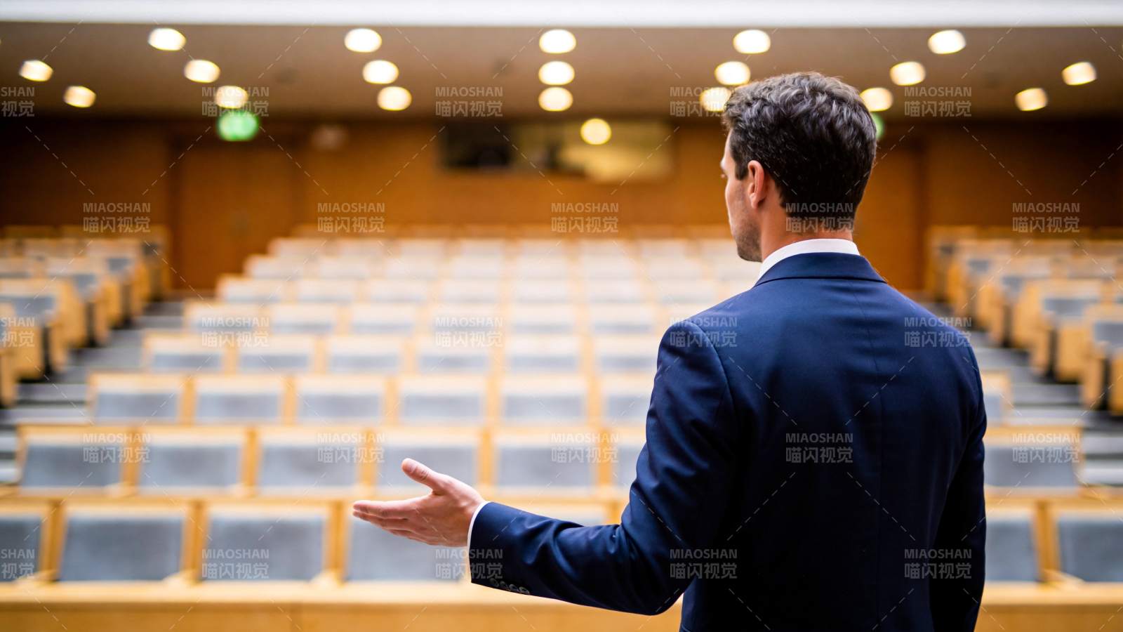 男士背对镜头在空旷讲堂中演讲手势示意图片