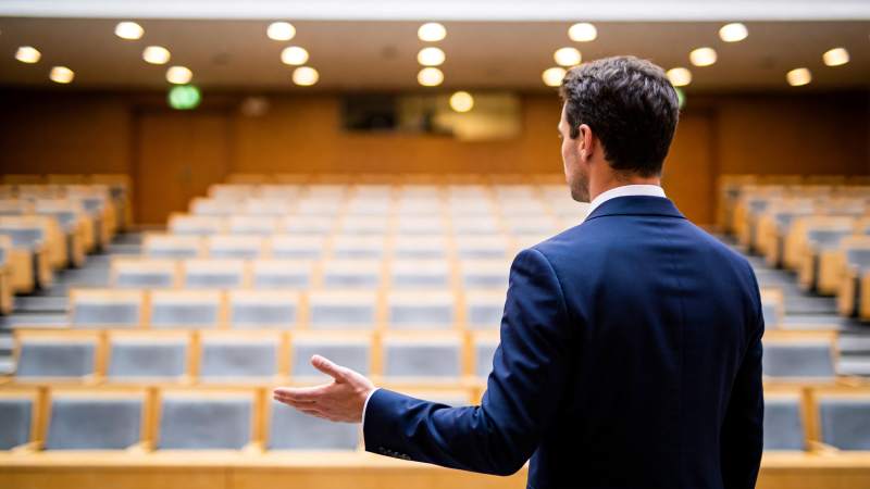 男士背对镜头在空旷讲堂中演讲手势示意图片
