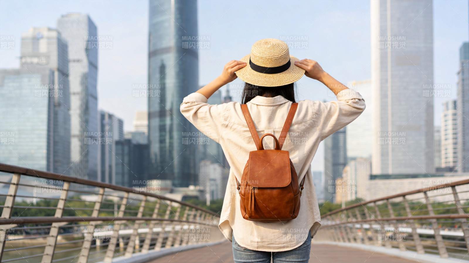 女子戴草帽背背包站在城市天桥远望高楼图片