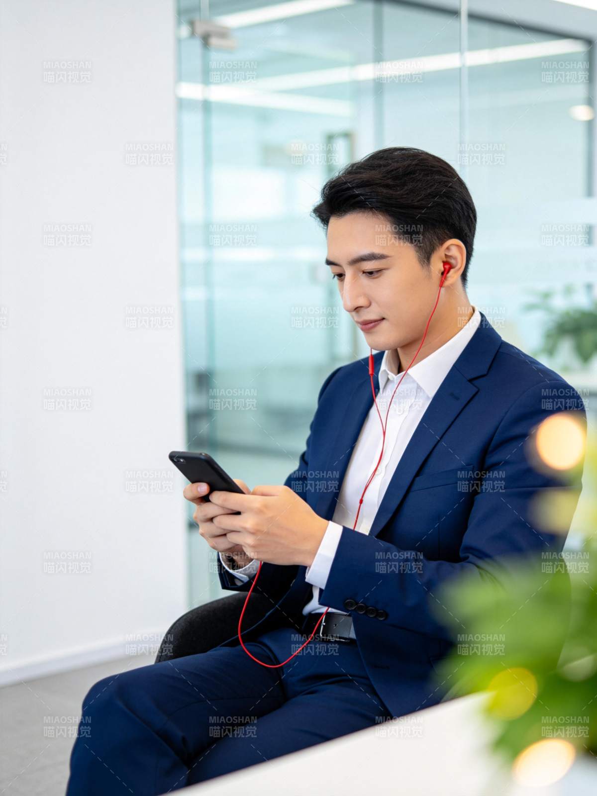 穿深蓝西装男子坐椅用手机听红耳机图片