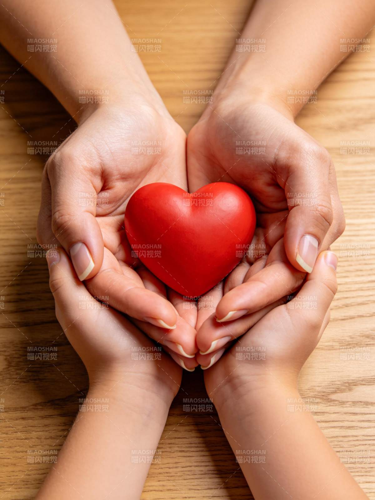 双手捧着红色心形物体置于木桌之上图片