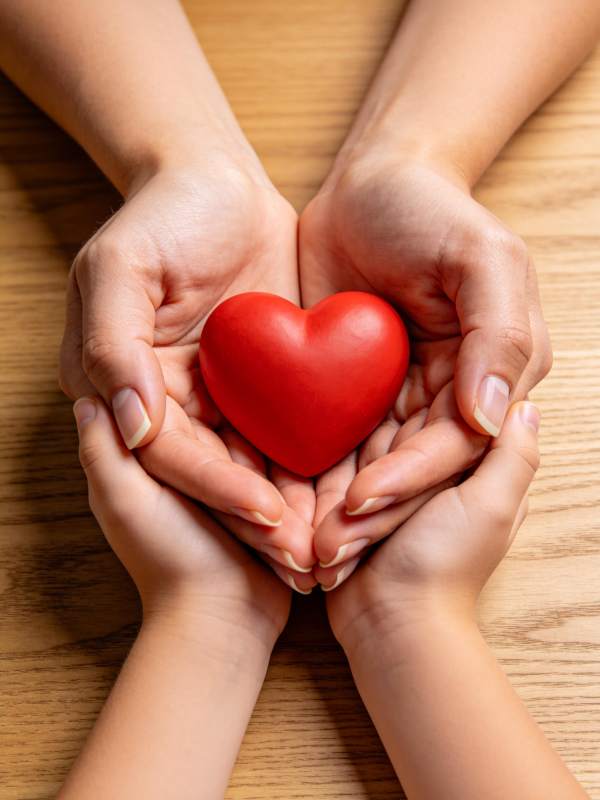 双手捧着红色心形物体置于木桌之上图片