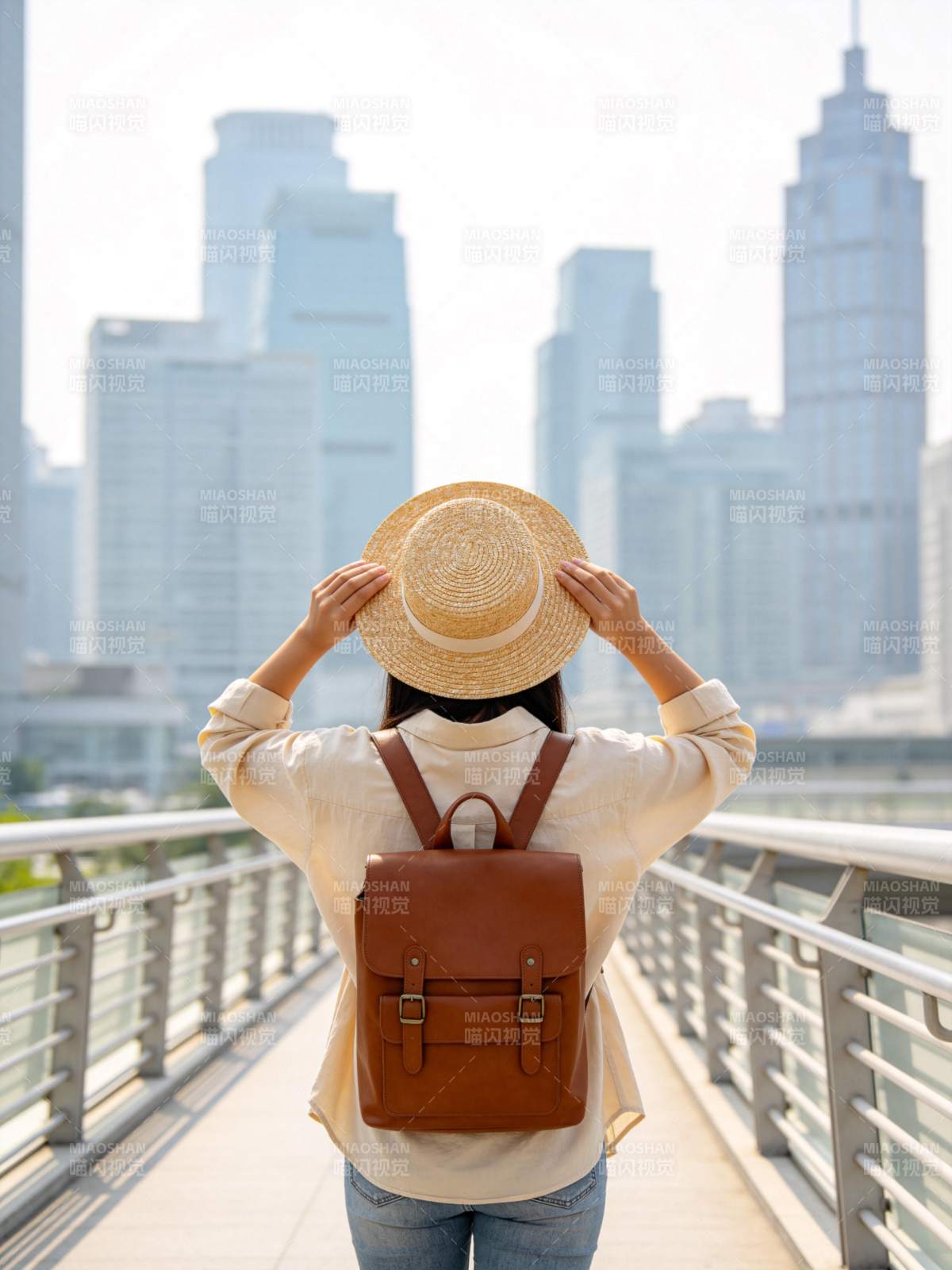 女子背背包戴草帽站在城市天桥远望高楼图片