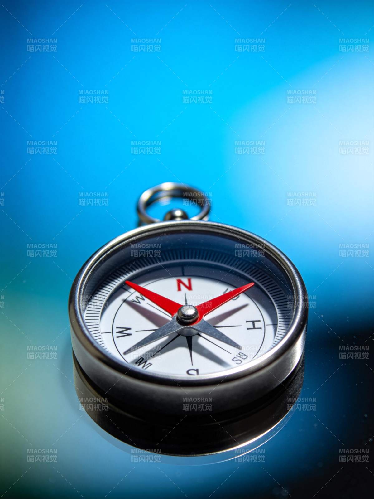 金属指南针置于蓝色渐变背景上特写图片