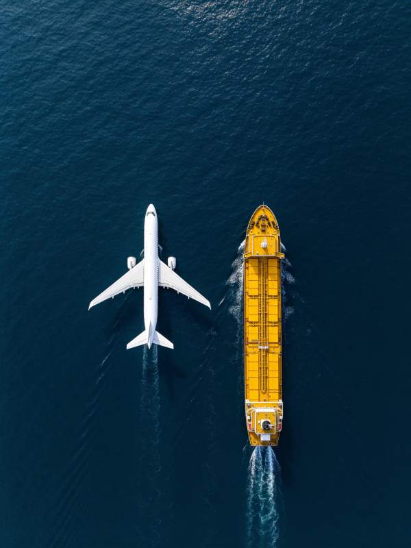 白色客机与黄色货轮并行航行于深蓝海面图片