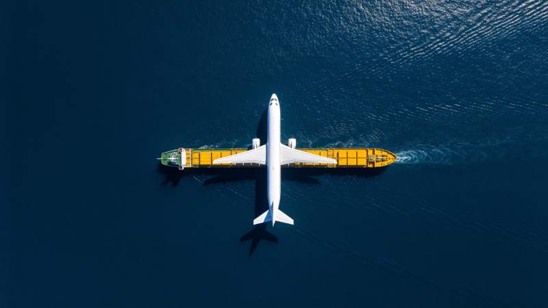飞机与货轮在深蓝海面并行航行图片