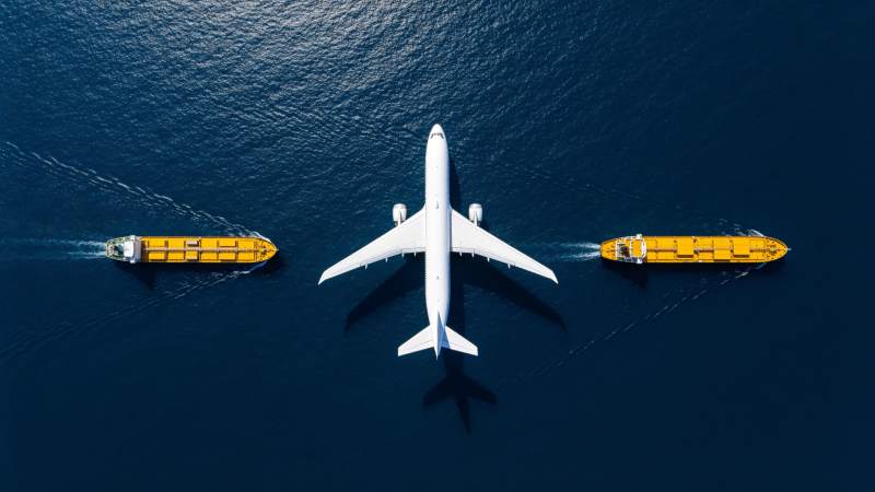 白色客机与两艘黄色货船在深蓝海面航行图片