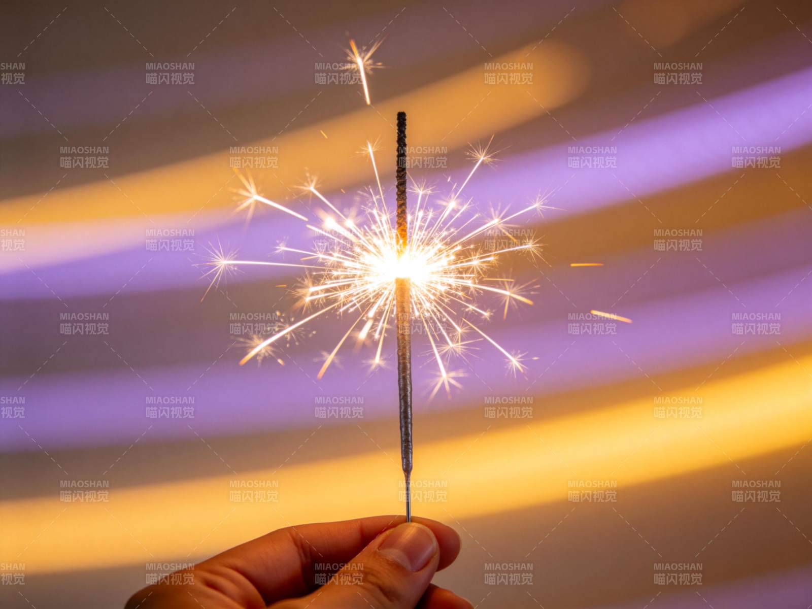 手持点燃的烟花棒在彩色光带背景前图片