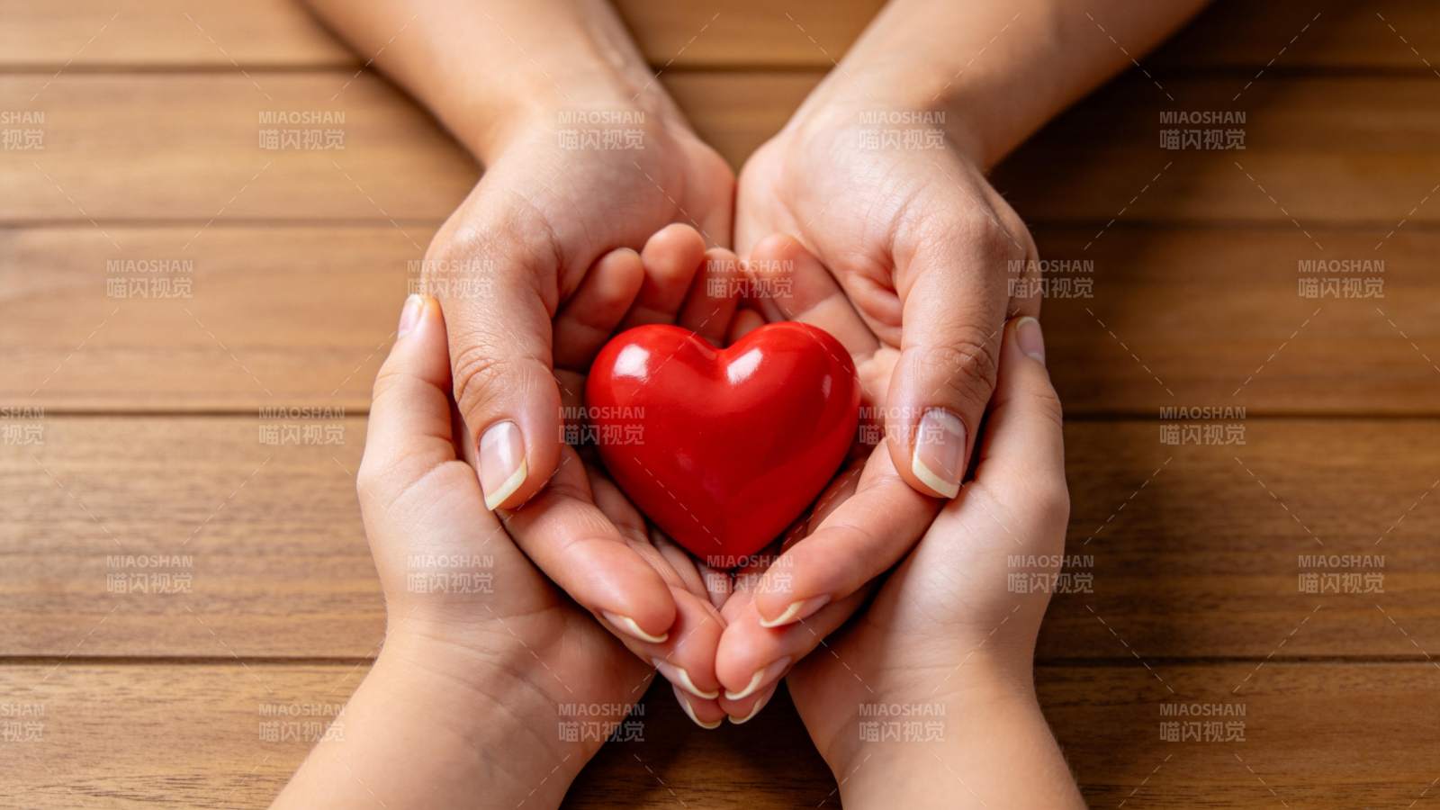 四只手共同托举红色心形物体置于木桌之上图片